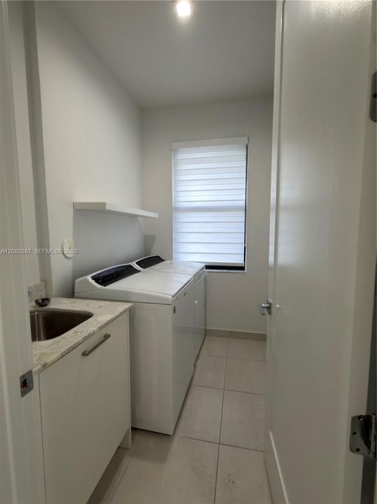 Utility room featuring tile flooring, built-in cabinetry with a stone-finish countertop, an integrated sink, a wall-mounted floating shelf, and a window with a roller shade
