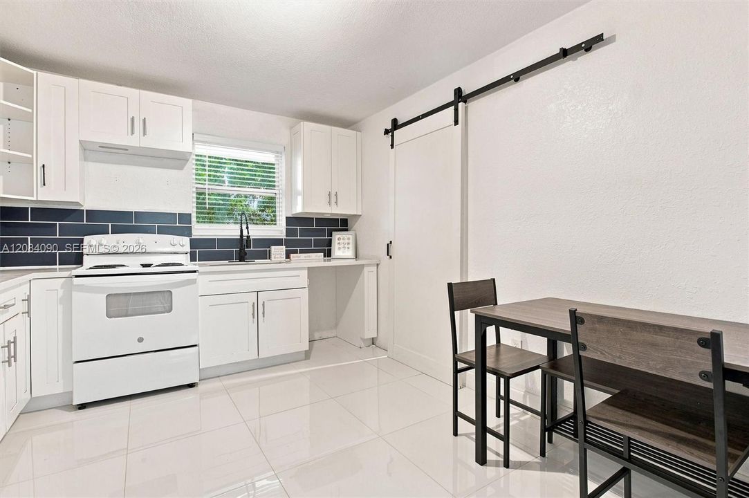 Bright eat-in kitchen with white cabinetry, modern backsplash, ample counter space, and a stylish barn door leading to the laundry area.