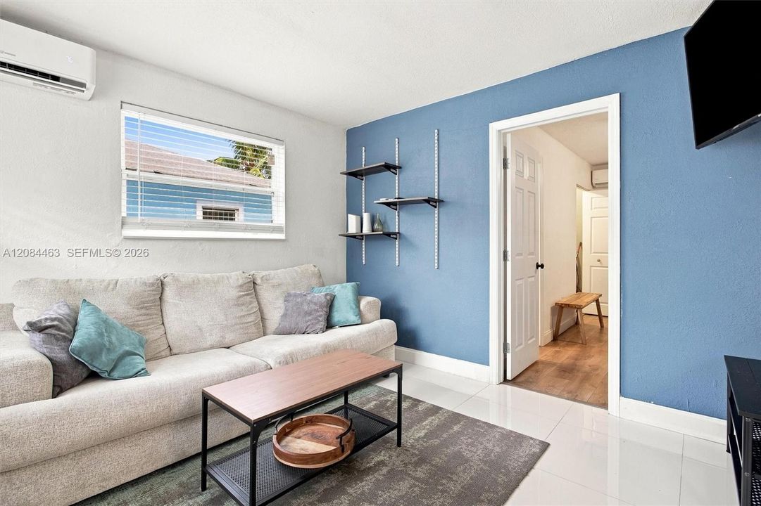 Cozy, fully furnished living area featuring a comfortable sofa, coffee table, wall-mounted TV, and decorative shelving. A bright, inviting, move-in-ready space