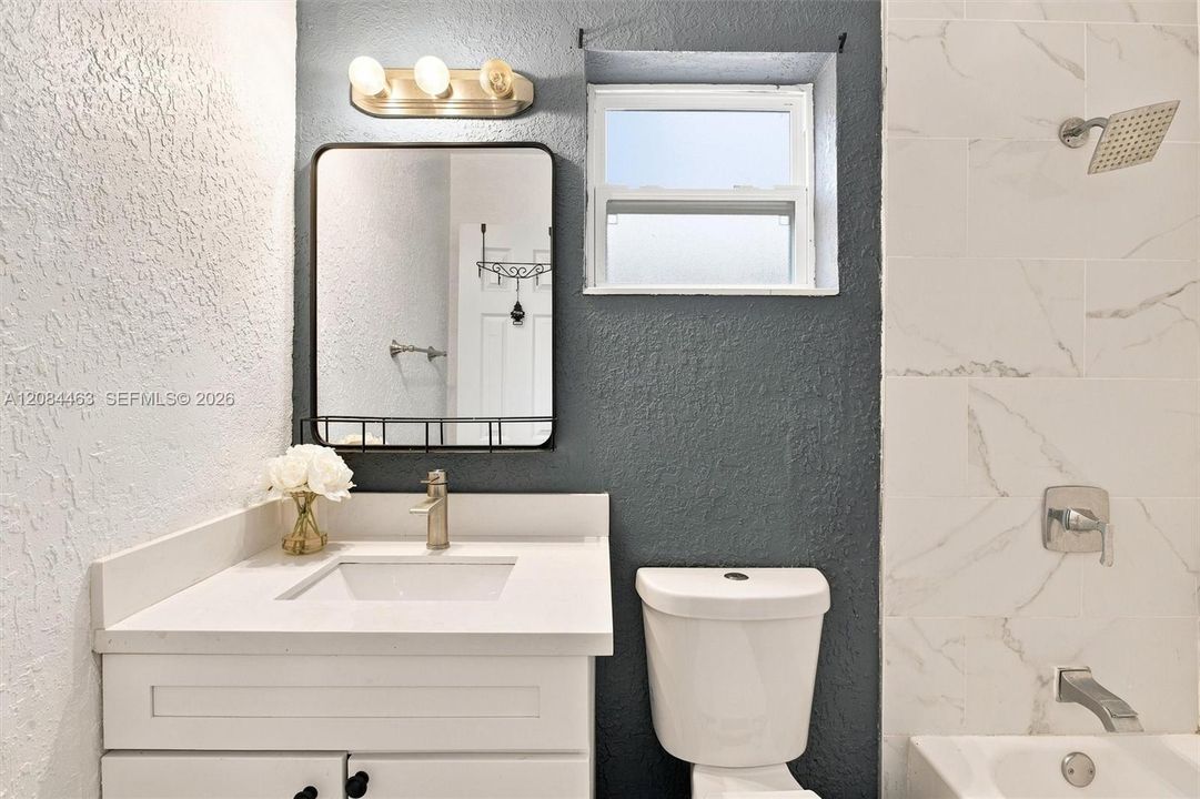 Updated bathroom featuring a sleek vanity, modern fixtures, marble-look tile, rainfall shower, and natural light for a fresh, contemporary feel.