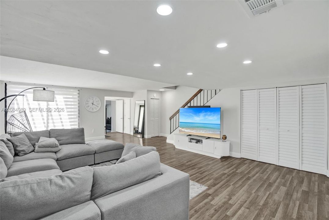 Living area featuring wood-finish flooring, recessed lighting, multi-panel louvered closet doors, and a staircase with a wooden handrail and metal balusters