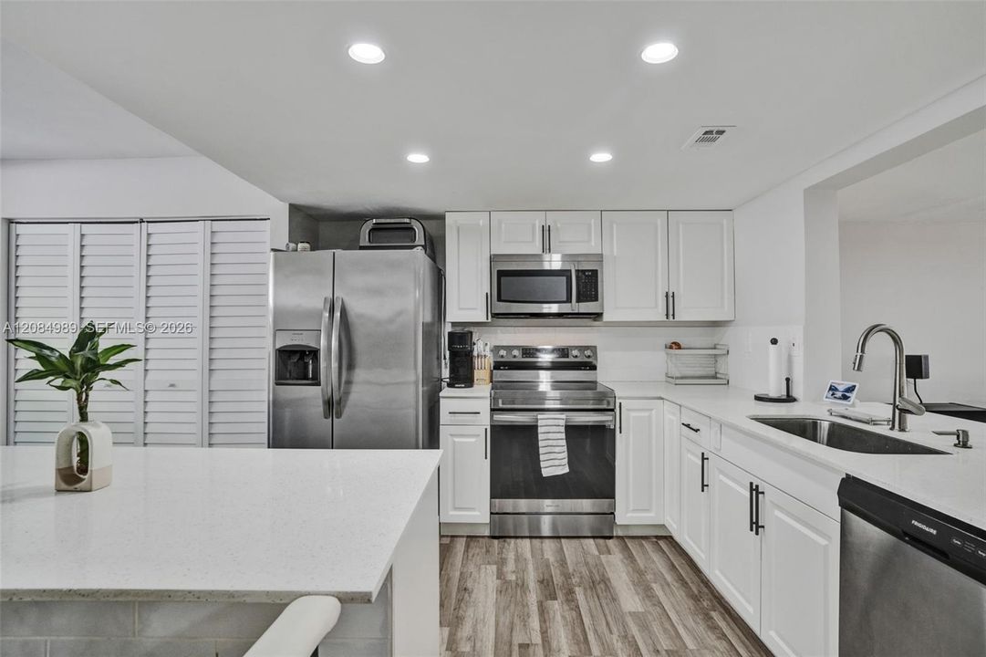 Kitchen featuring white shaker-style cabinetry, solid-surface countertops, recessed lighting, wood-finish flooring, and stainless steel appliances