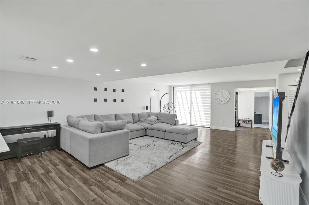 Open-concept interior featuring wood-finish flooring, recessed lighting, and a large sliding glass door with horizontal blinds