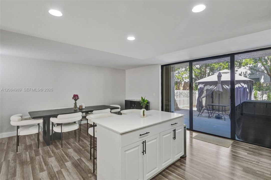 Kitchen island with a white countertop and base cabinetry, wood-finish flooring, recessed lighting, and expansive black-framed sliding glass doors