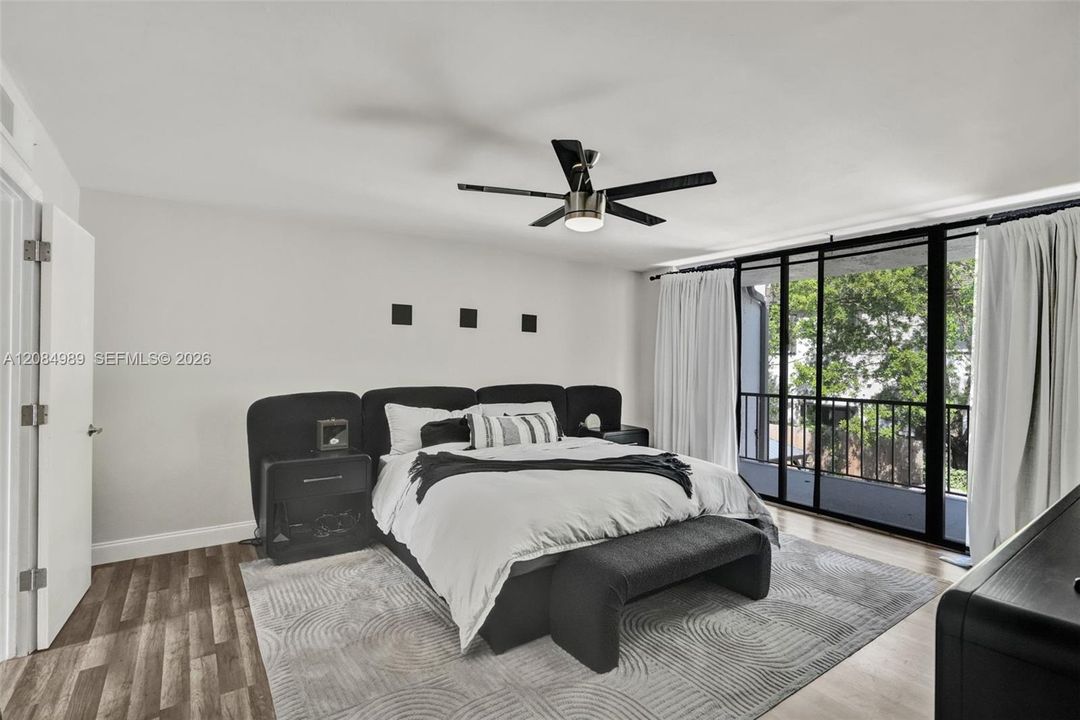 Room featuring wood-finish flooring, a matte black multi-blade ceiling fan with integrated lighting, and floor-to-ceiling sliding glass doors opening to a private balcony