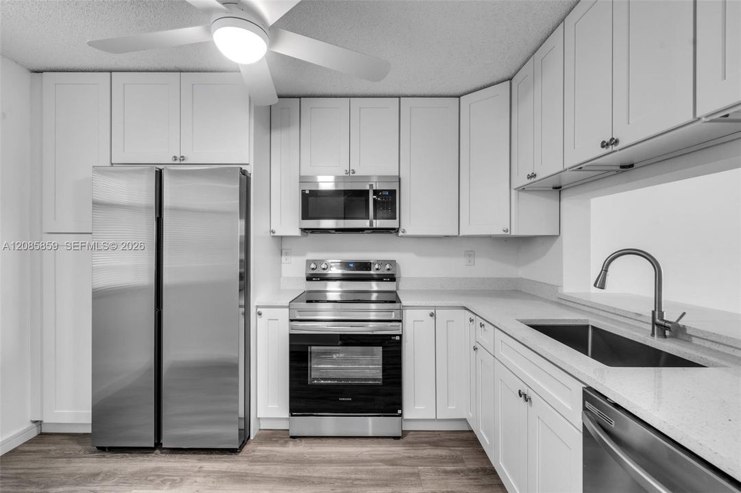 Updated kitchen equipped with clean white cabinetry, modern grey countertops, and sleek stainless steel appliances.