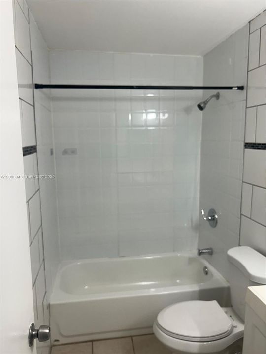 Bathtub and shower combination featuring white tile surround with dark horizontal accent detailing, chrome-finish plumbing fixtures, and standard-height toilet