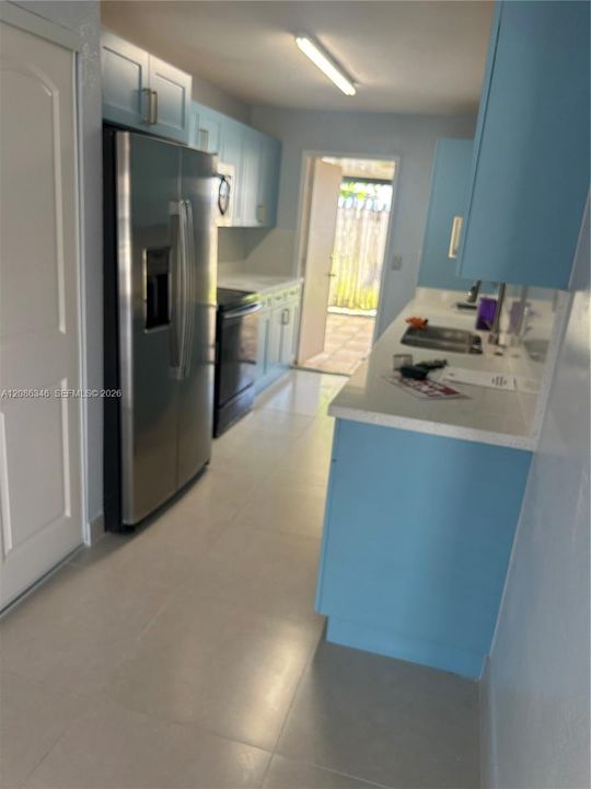 Kitchen featuring light blue cabinetry, solid surface countertops, stainless steel side-by-side refrigerator, dual-basin stainless steel sink, and light-toned tile flooring