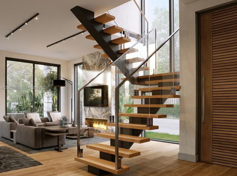 Floating staircase with wood treads and glass railing, wide plank wood-finish flooring, full-height windows, built-in fireplace with stone surround, and flush-mounted ceiling lighting