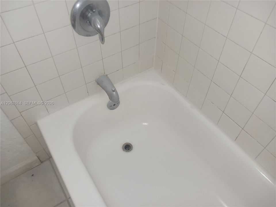 Bathtub featuring a white finish, surrounding square-tile wall cladding, and metal shower-and-tub plumbing fixtures