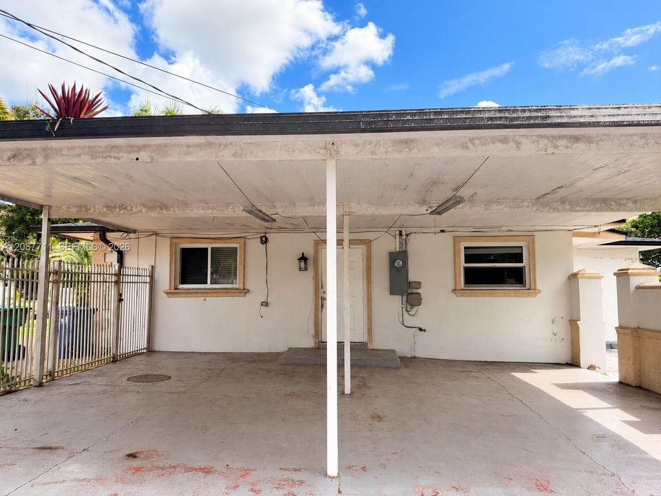 Covered carport featuring a concrete floor, metal support columns, integrated lighting fixtures, and decorative masonry pillars