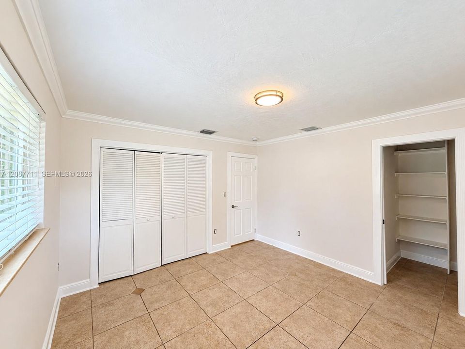 Room featuring tile flooring, crown molding, a multi-panel door, built-in louvered-style closet doors, and a reach-in storage area with fixed shelving