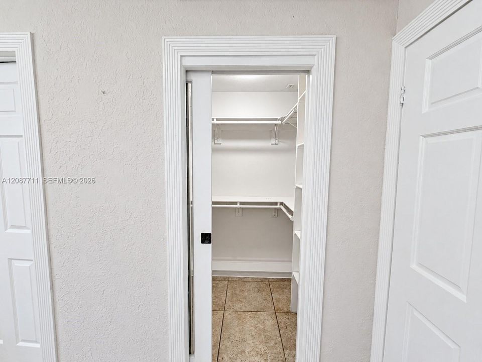 Walk-in closet featuring a sliding door, tiered white shelving, and tiled flooring