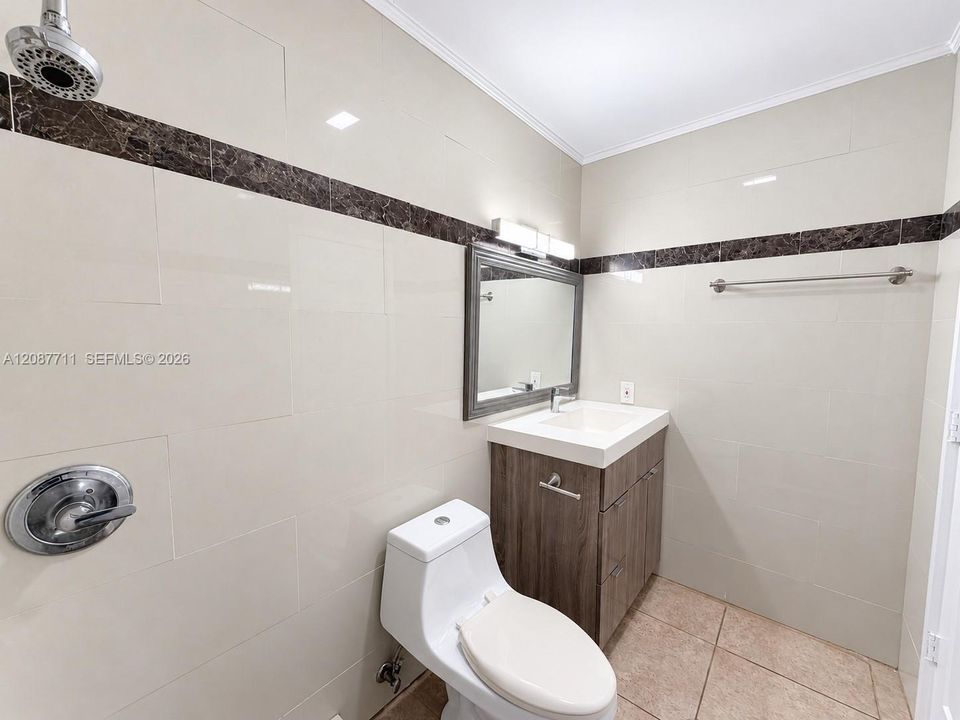 Bathroom featuring light-toned wall tile with dark stone accent trim, wood-finish vanity with a rectangular sink, wall-mounted light fixture, and metal towel bar