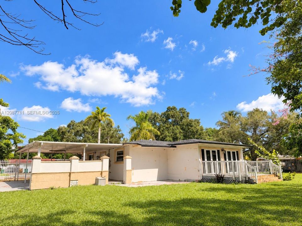 Single-story residence featuring an attached carport, covered side porch with decorative pillars, white railing, and a spacious lawn