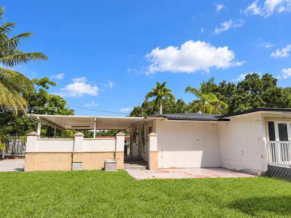 Rear exterior featuring a covered patio, stucco and masonry wall, integrated carport, concrete flooring, and manicured lawn
