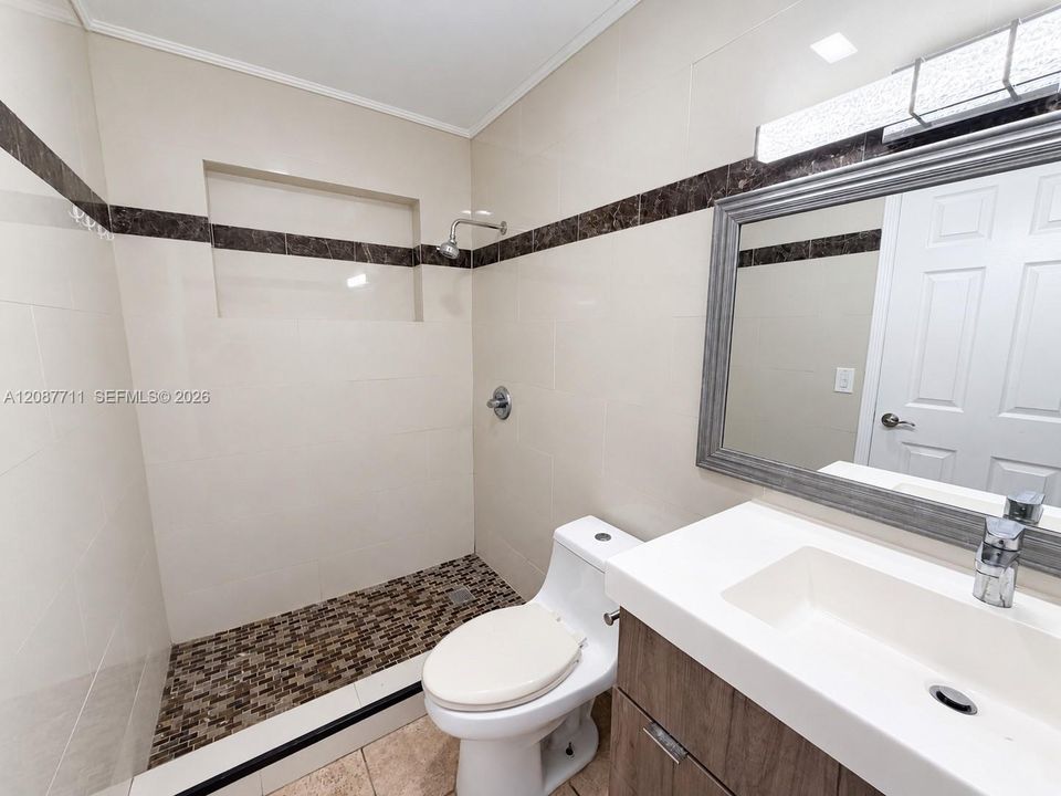 Bathroom featuring large-format wall tile with decorative stone inlay, a walk-in shower with stone mosaic flooring and built-in recessed shelving, and a vanity with a white integrated sink and wood-finish cabinetry
