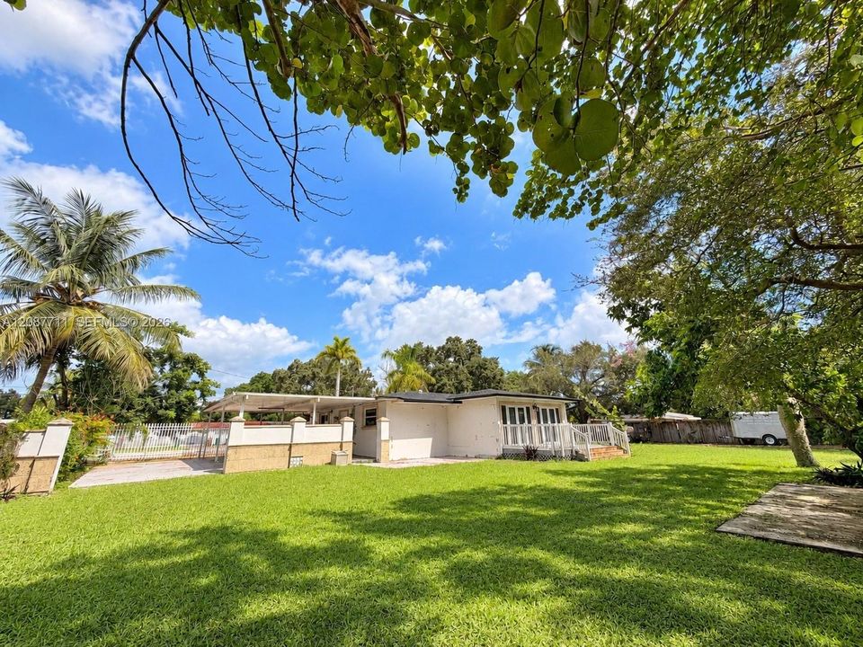 Expansive lawn featuring mature trees, a covered patio, and perimeter masonry wall