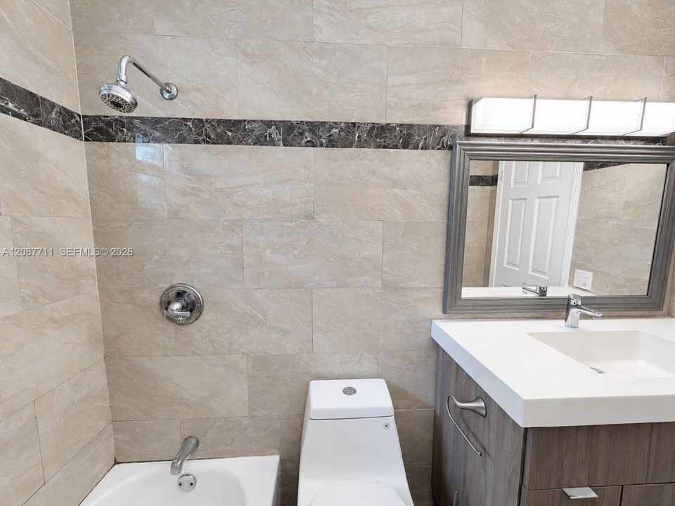 Bathroom featuring floor-to-ceiling tile with a contrasting decorative inlay, a wood-finish vanity with a white countertop and integrated sink, a contemporary multi-light fixture, and a framed mirror