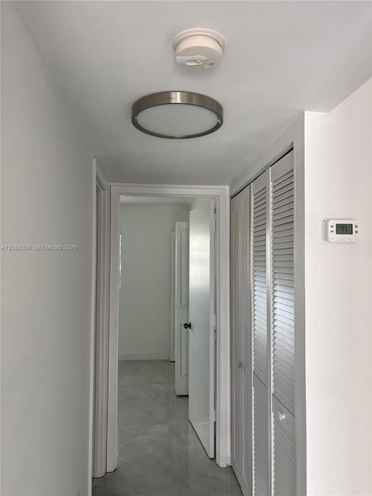 Neutral interior hall featuring louvered bi-fold closet doors, a contemporary circular flush-mount ceiling light, and stone-finish flooring