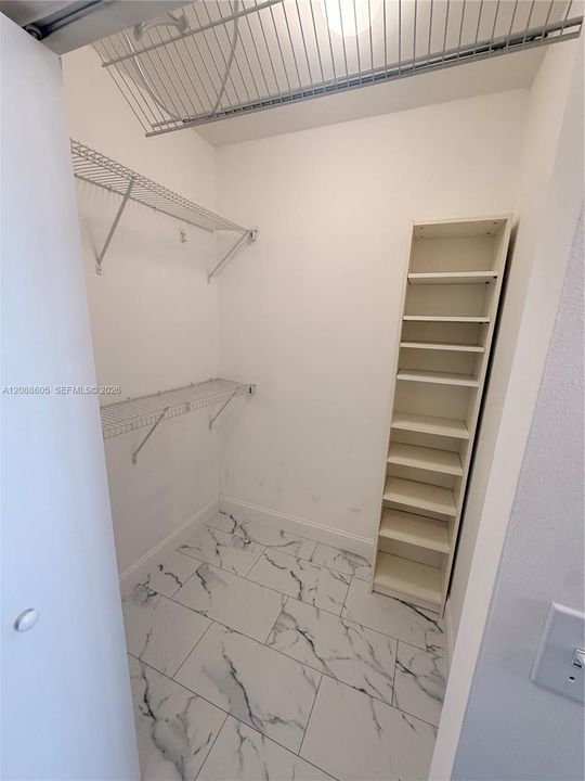 Storage space featuring tile flooring with a marble-patterned finish, multi-level wire shelving, and built-in vertical shelving unit