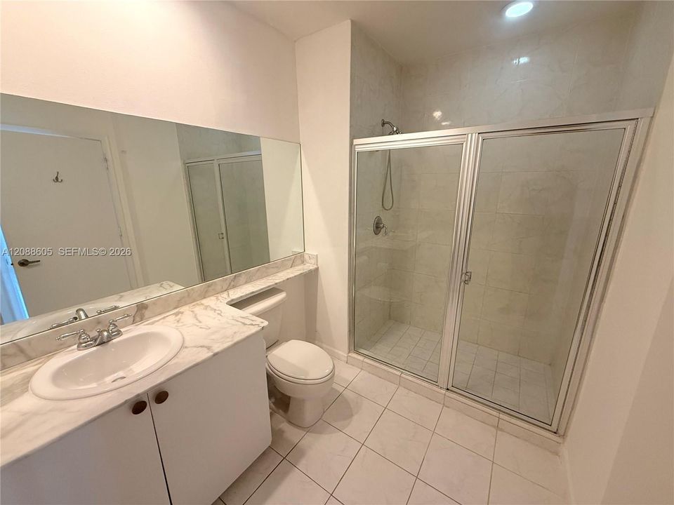 Bathroom featuring a stone-top vanity with an integrated basin, large wall-mounted mirror, walk-in shower with a glass enclosure, and tile flooring