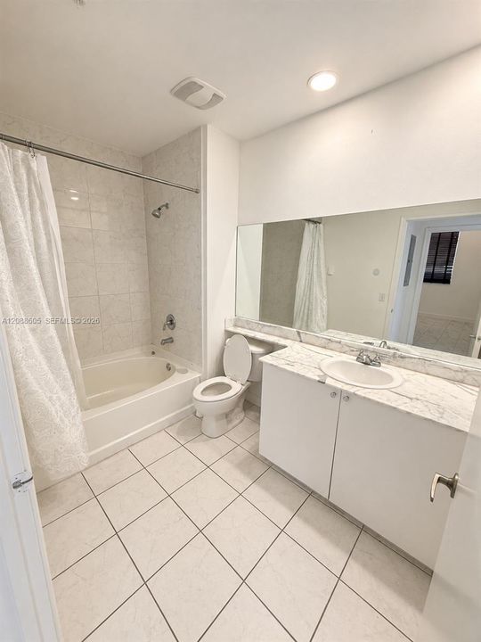 Bathroom featuring a vanity with an integrated basin, stone-finish countertop, full-width wall mirror, tile flooring, and a shower-tub combination with tile surround