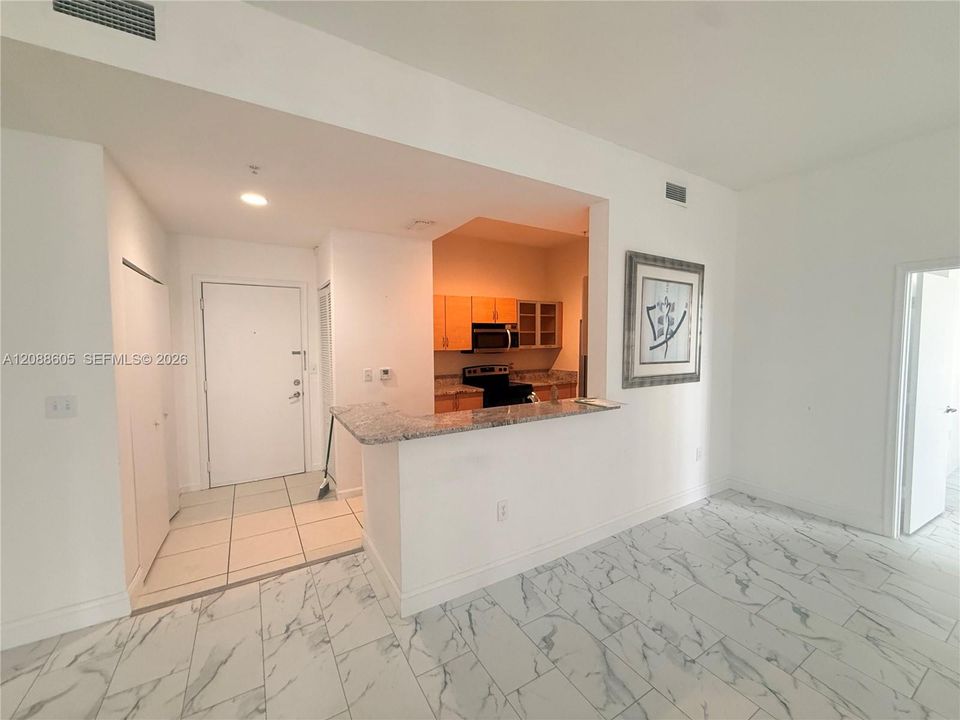 Open-concept kitchen featuring a breakfast bar with stone-look countertop, light wood cabinetry, built-in microwave, and stone-look tile flooring