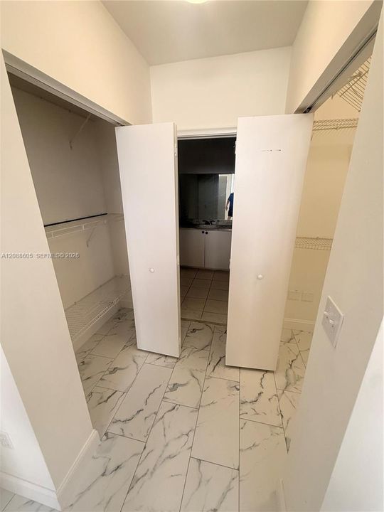 Walk-in closet featuring large-format tile flooring with a veined pattern, dual bifod doors, and installed wire shelving