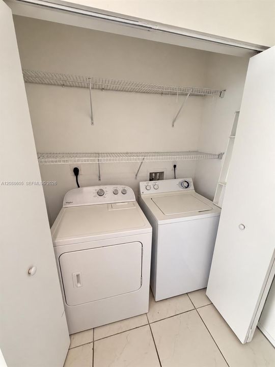 Laundry closet featuring built-in dual-tier wire shelving, tile flooring, and dedicated hookups for a washer and dryer