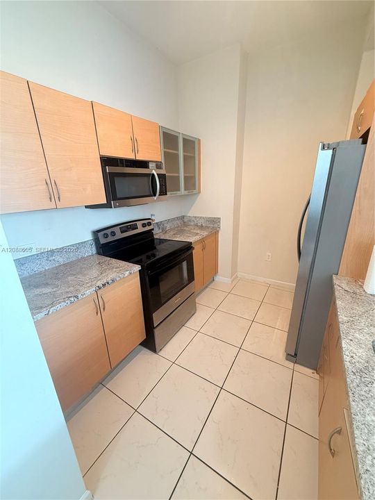 Kitchen featuring light-finish cabinetry, stone-patterned countertops, stainless steel appliances, and tile flooring
