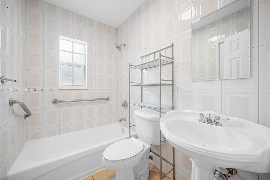 Full bathroom complete with standard bathtub/shower combination, classic wall tiling, and pedestal sink.