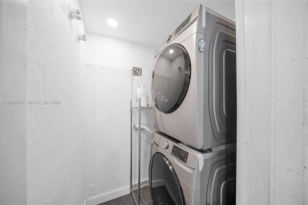 Convenient interior laundry room equipped with a full-size stacked washer and dryer plus utility room storage space.