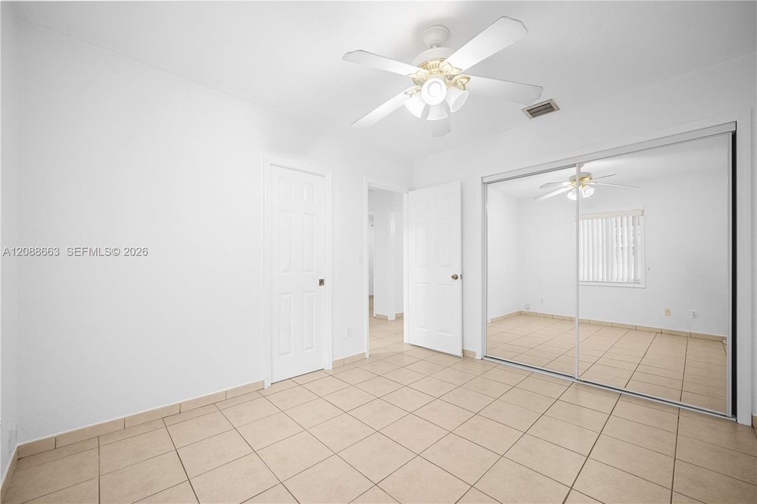 Generous primary bedroom with central AC, ceiling fan, ceramic tile floors, and custom mirrored closet doors.