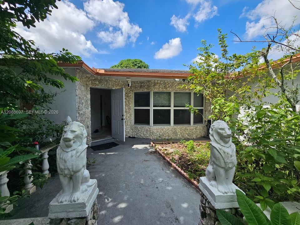 Exterior entrance featuring natural stone veneer, concrete walkway, and decorative stone-finish pedestals