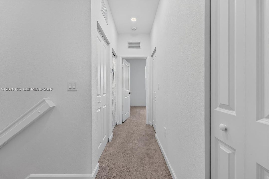 Hallway featuring neutral carpeting, multiple interior doors with round hardware, and recessed lighting