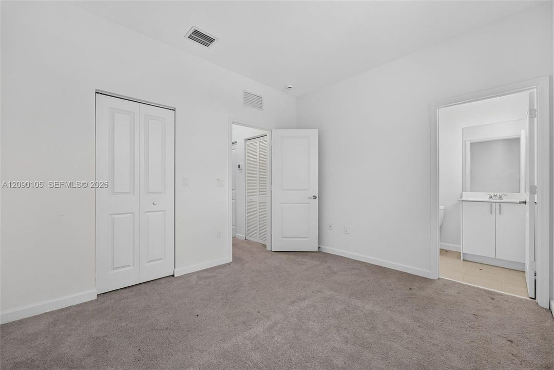 Room featuring neutral carpeting, white interior doors, dual-panel closet doors, and direct access to an ensuite with a white vanity