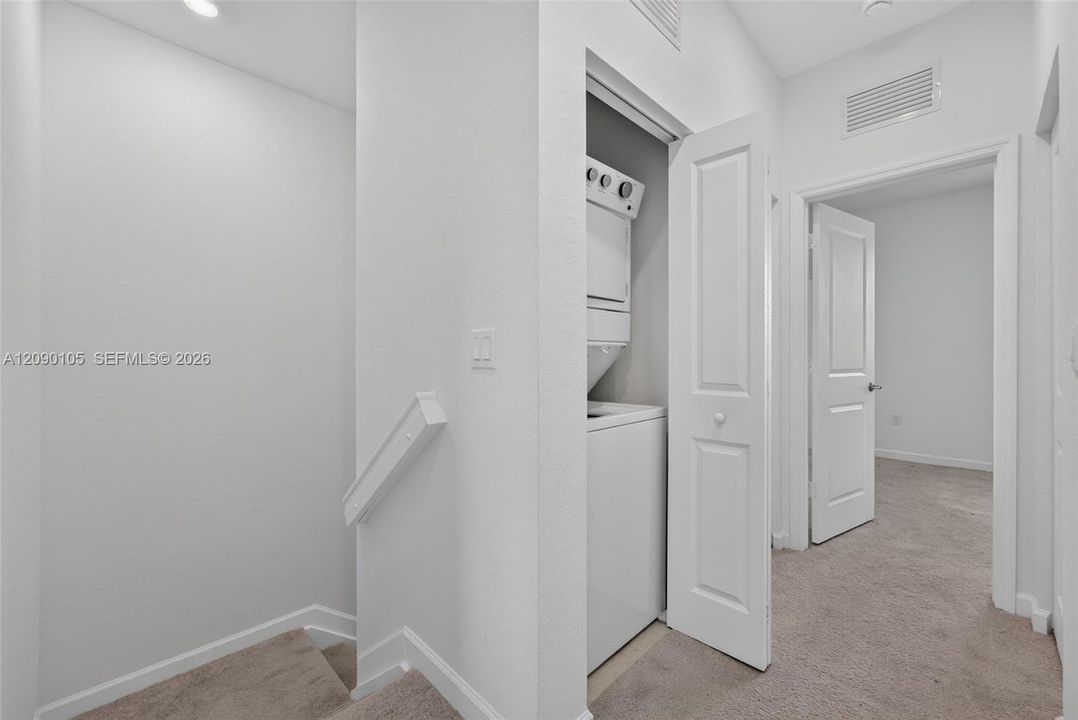 Stacked laundry unit housed in a dedicated closet featuring a solid-panel door, neutral carpeting, and multi-panel interior doors