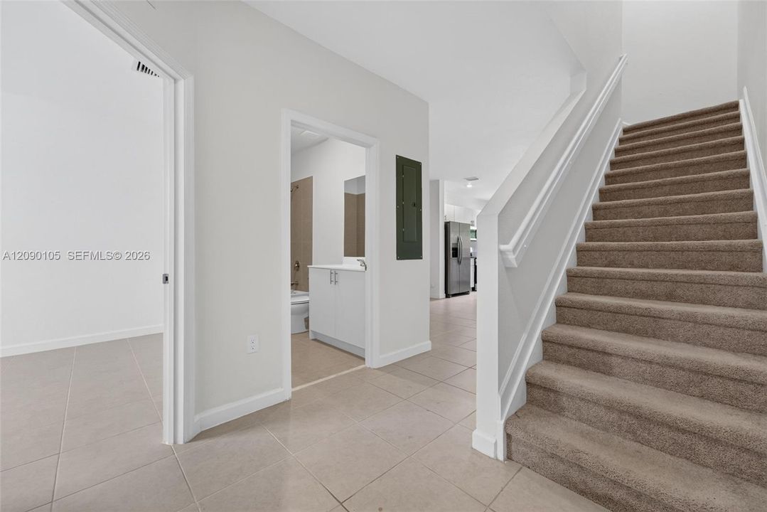 Foyer featuring large-format ceramic tile flooring, a carpeted staircase with white handrails, and a vanity with a white basin and cabinet