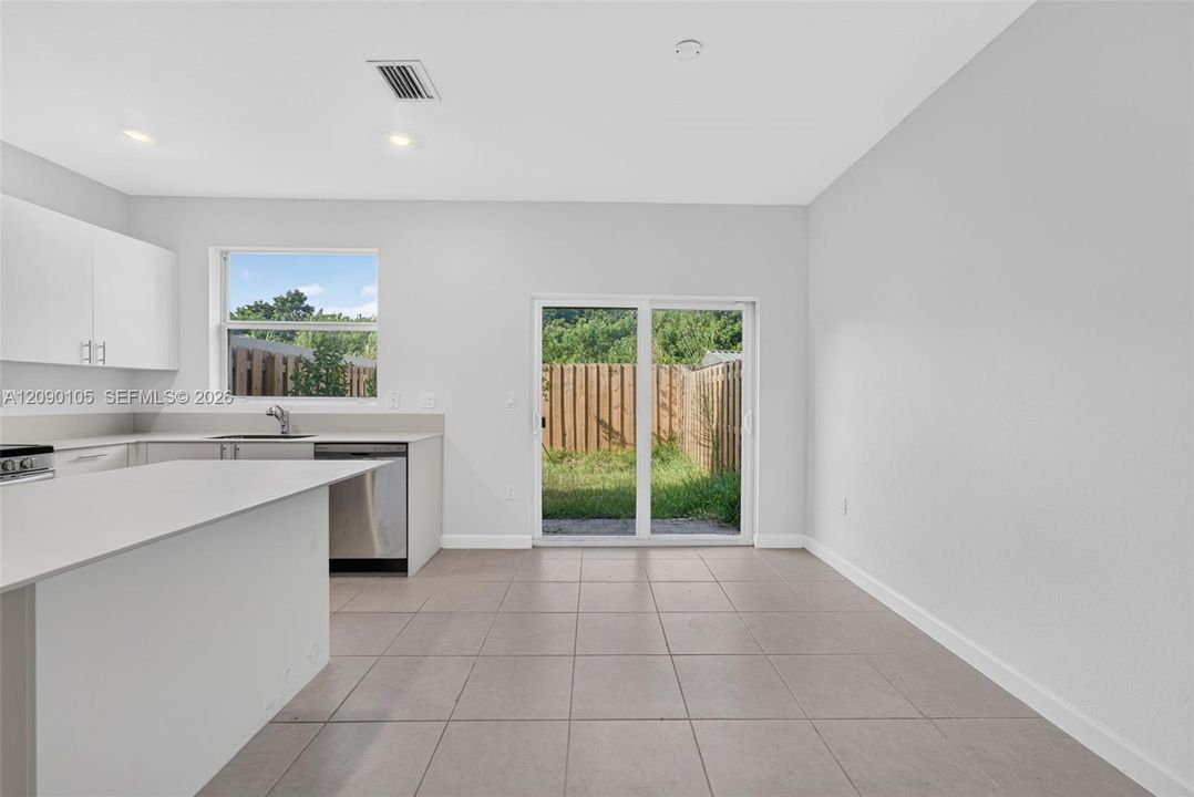 Kitchen featuring a peninsula with solid-surface countertops, white cabinetry, stainless steel appliances, large-format tile flooring, and sliding glass doors leading to a fenced outdoor area