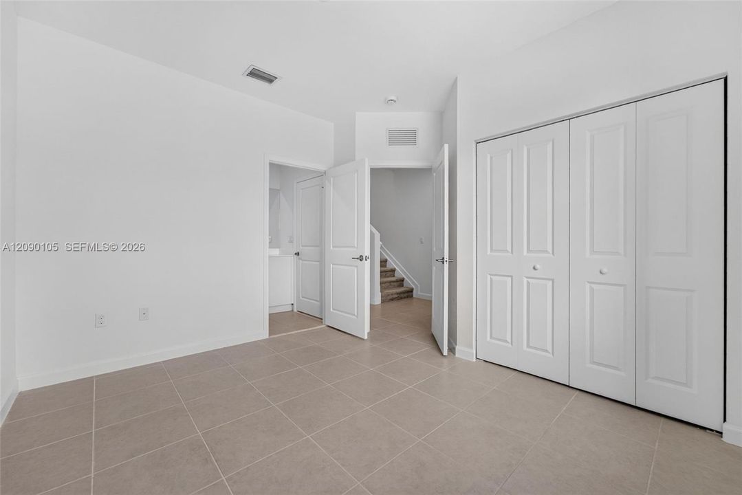 Neutral tile flooring, multi-panel interior doors, and a double-door closet with white finish