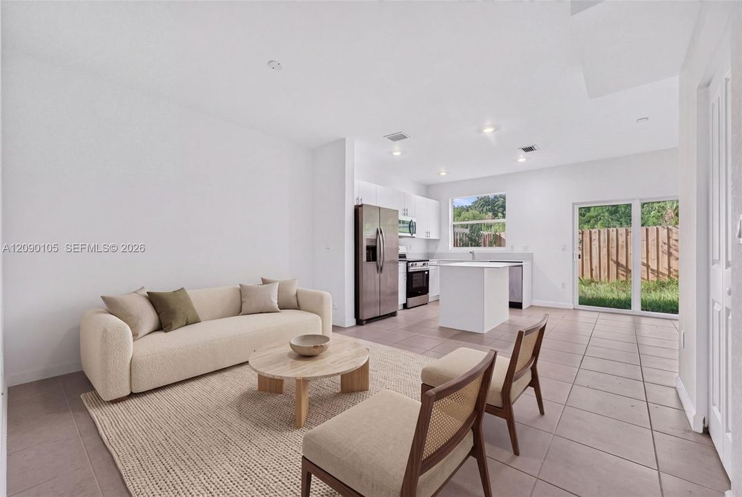 Open-concept interior featuring large-format ceramic tile flooring, a kitchen with white cabinetry and a central island, stainless steel appliances, recessed lighting, and sliding glass doors