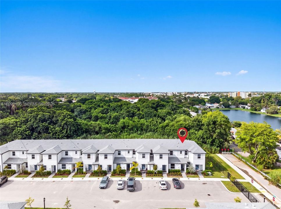 Multi-unit residential complex featuring gabled rooflines, light-toned exterior finish, ground-level entryways, and asphalt parking area