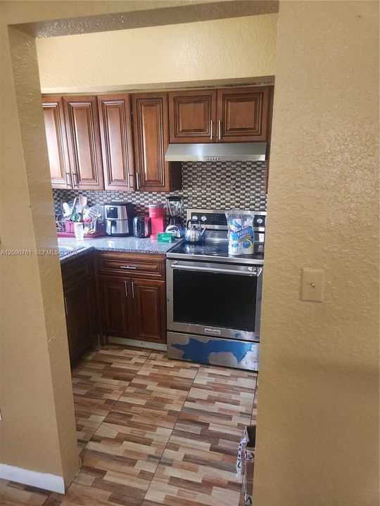 Kitchen featuring wood cabinetry, stone-finish countertops, stainless steel range with overhead vent hood, tiled backsplash, and patterned tile flooring
