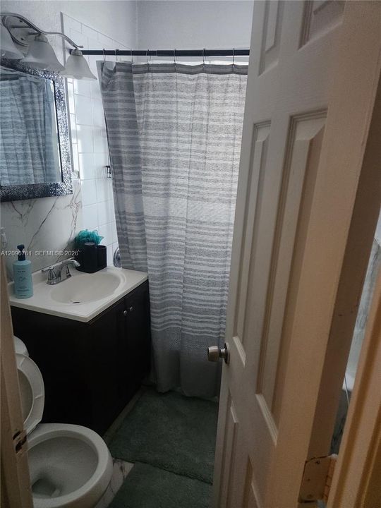 Bathroom featuring a vanity with an integrated sink, stone-patterned wall surfacing, a multi-light fixture, and a combination shower and tub enclosure