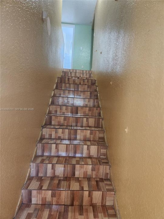 Staircase featuring tiled treads and risers with a multi-toned, wood-finish pattern and textured wall surfaces