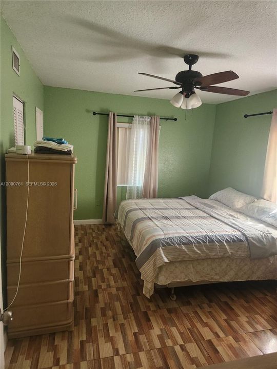 Room featuring wood-finish flooring, a multi-blade ceiling fan with integrated light fixture, and two windows with mounted curtain rods