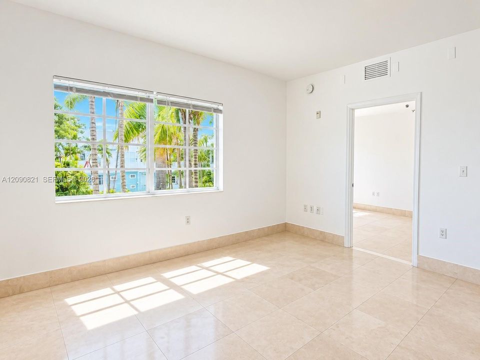 Sunlit bedroom with large window and generous floor space.