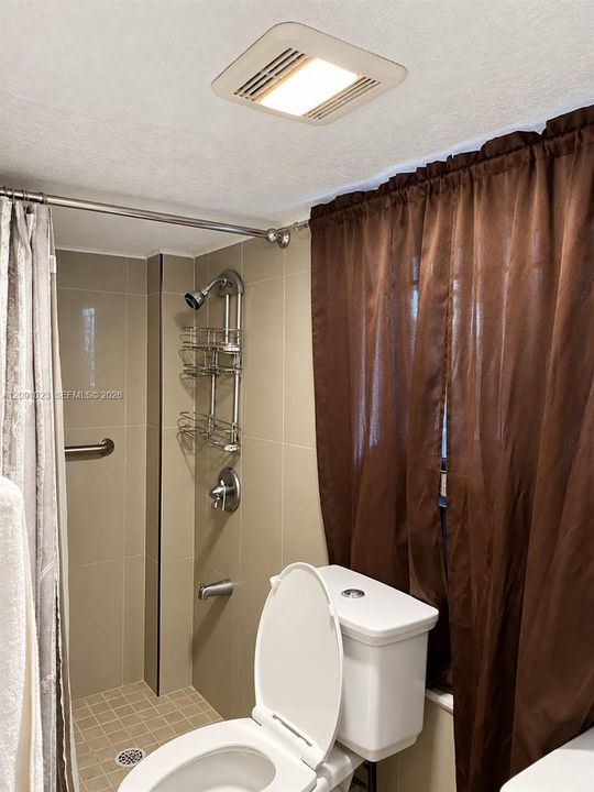 Full-height neutral wall tiling, integrated tub and shower combination with chrome fixtures, mosaic-tiled shower floor, and recessed ceiling lighting