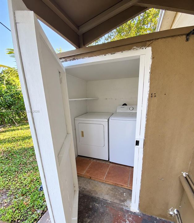 Dedicated exterior laundry alcove featuring white appliance enclosures, tile flooring, and integrated storage shelving